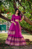 Woman wearing a premium royal purple cotton silk Chaniya Choli with a traditional gold zari border standing outdoors at a festive event boutique location.