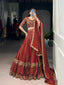 Model showcasing a premium royal rust silk Chaniya Choli featuring heavy antique gold zari and dori floral panel embroidery, an intricately detailed matching elbow sleeve blouse, and a scalloped border dupatta inside a boutique showroom.