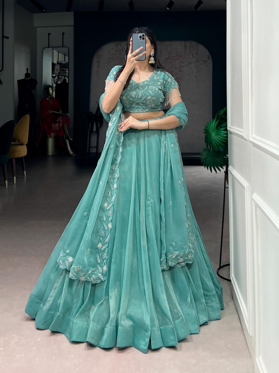 Model showcasing a premium mint green georgette Chaniya Choli featuring a wide solid hem border, a heavily embroidered short-sleeve blouse, and a matching scalloped border dupatta inside a boutique showroom.