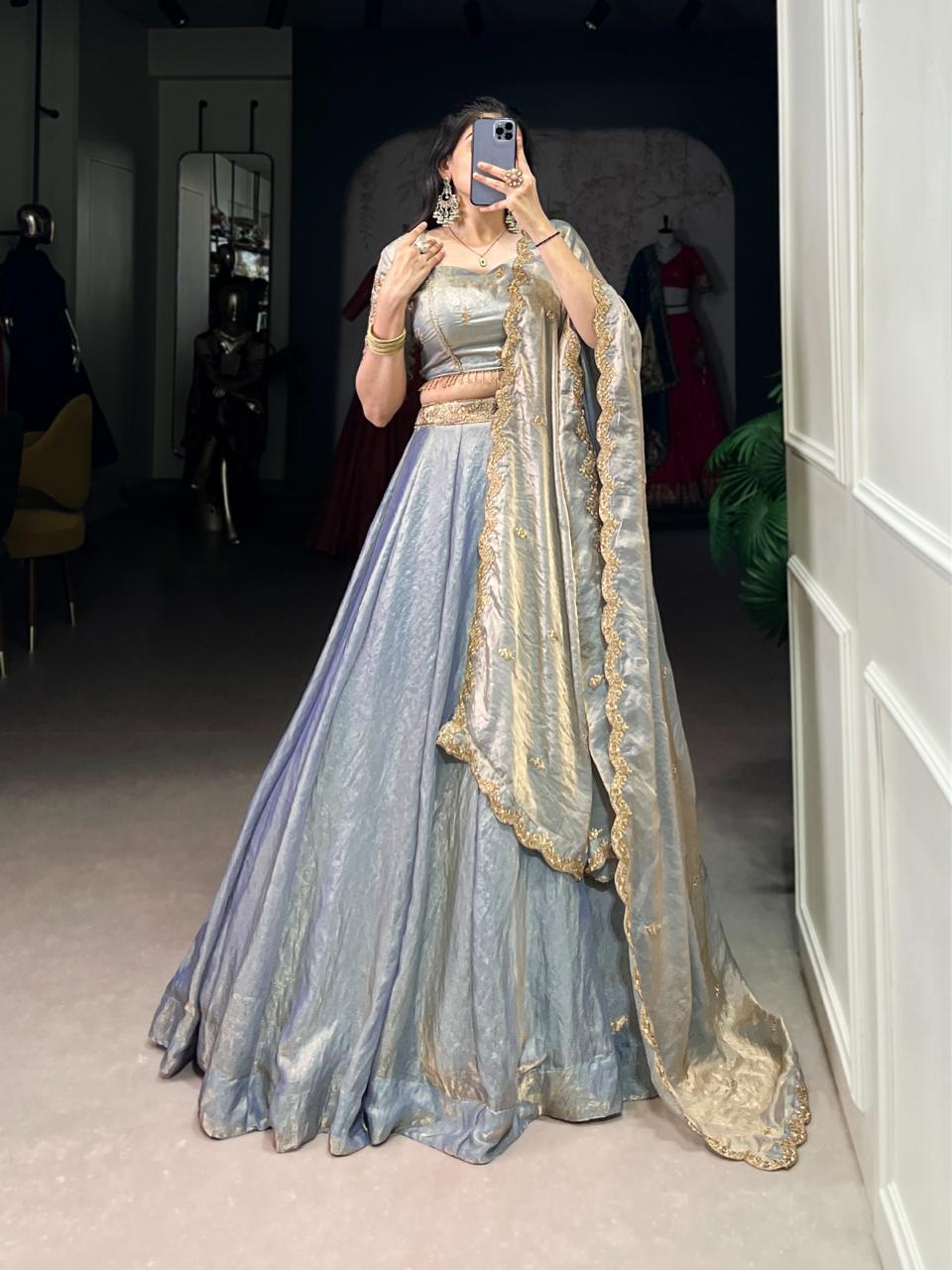 Model showcasing a premium ice blue metallic tissue silk Chaniya Choli featuring a dual-tone gold shimmer, matching sleeveless choli blouse, and a heavy scalloped gold zari border dupatta inside a boutique. Main image