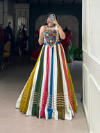 Model showcasing a premium multi-color panel structured Chaniya Choli with horizontal gold gota laces and an authentic heavily embroidered Kutchi Gamthi mirror work corset blouse inside a boutique store.