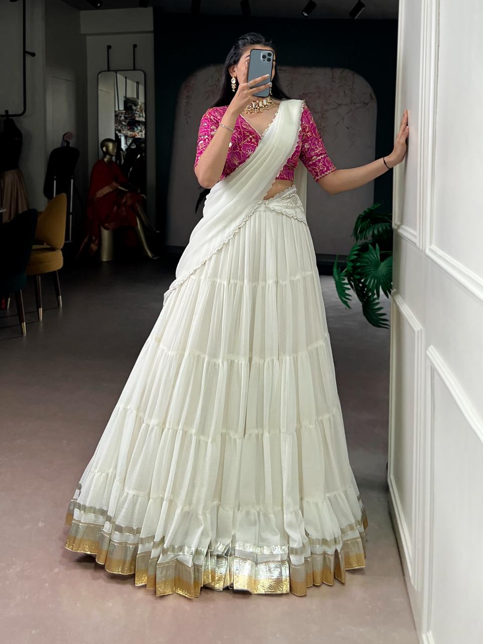 Model showcasing a premium off-white tiered georgette Chaniya Choli in a saree-drape style, featuring wide gold and silver zari border hem bands, a contrasting magenta pink floral brocade blouse, and a scalloped border drape inside a boutique showroom. Main image