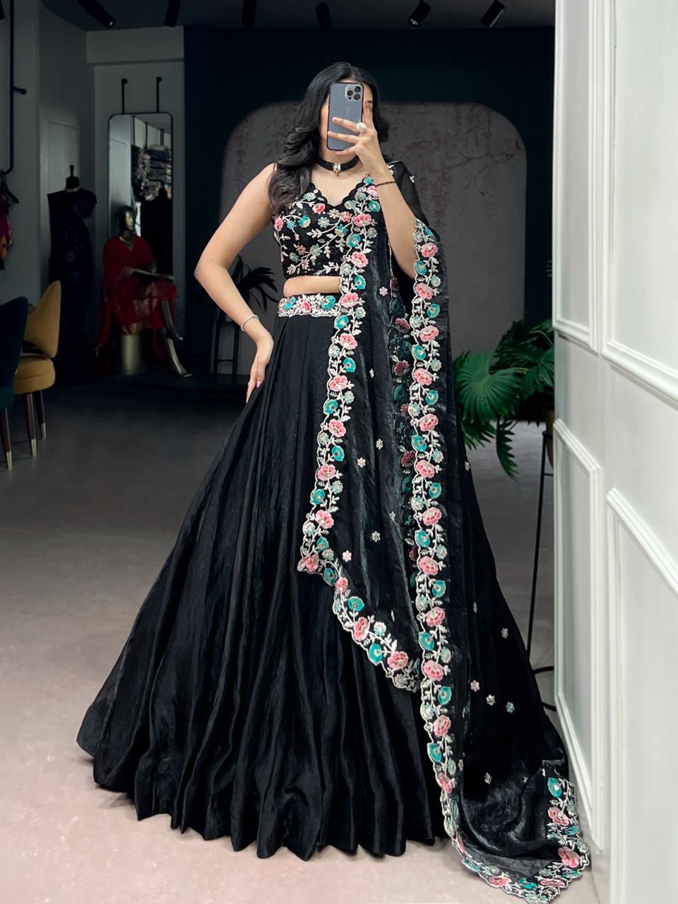 Model showcasing a premium jet black silk Chaniya Choli featuring a matching embroidered waistband, a heavily detailed pastel pink and sea green floral blouse, and a matching wide scalloped border dupatta inside a boutique showroom.