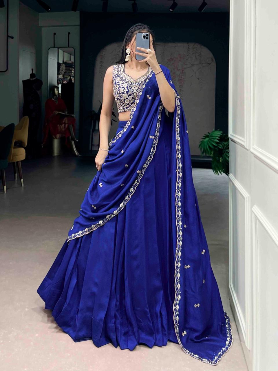 Model showcasing a premium royal blue georgette Chaniya Choli in a saree-drape style, featuring a heavily embroidered silver zardosi sleeveless blouse and a scalloped border dupatta inside a boutique showroom.