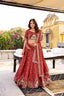 Model showcasing a premium brick red silk Chaniya Choli featuring an intricate traditional gold zari and resham palace-arch jharokha border embroidery, a matching heavily detailed blouse, and an embroidered dupatta inside a traditional heritage palace location.