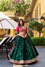Model showcasing a premium emerald green silk Chaniya Choli with a wide gold zari and hot pink floral embroidered border, paired with a heavily embellished contrasting hot pink silk blouse inside an outdoor luxury courtyard setting.