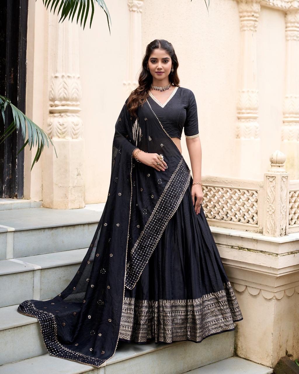 Model showcasing a premium royal midnight black cotton silk Chaniya Choli featuring a heavy woven gold zari border, an elegant V-neck elbow sleeve blouse, and an embroidered black dupatta inside a traditional architecture location. Main image