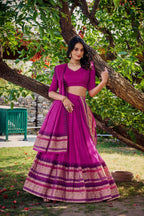 Woman wearing a premium royal purple cotton silk Chaniya Choli with a traditional gold zari border standing outdoors at a festive event boutique location.