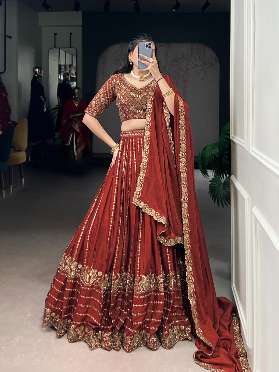 Model showcasing a premium royal rust silk Chaniya Choli featuring heavy antique gold zari and dori floral panel embroidery, an intricately detailed matching elbow sleeve blouse, and a scalloped border dupatta inside a boutique showroom. Main image