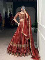 Model showcasing a premium royal rust silk Chaniya Choli featuring heavy antique gold zari and dori floral panel embroidery, an intricately detailed matching elbow sleeve blouse, and a scalloped border dupatta inside a boutique showroom.