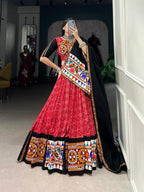 Person wearing a traditional red and black embroidered outfit in a room.