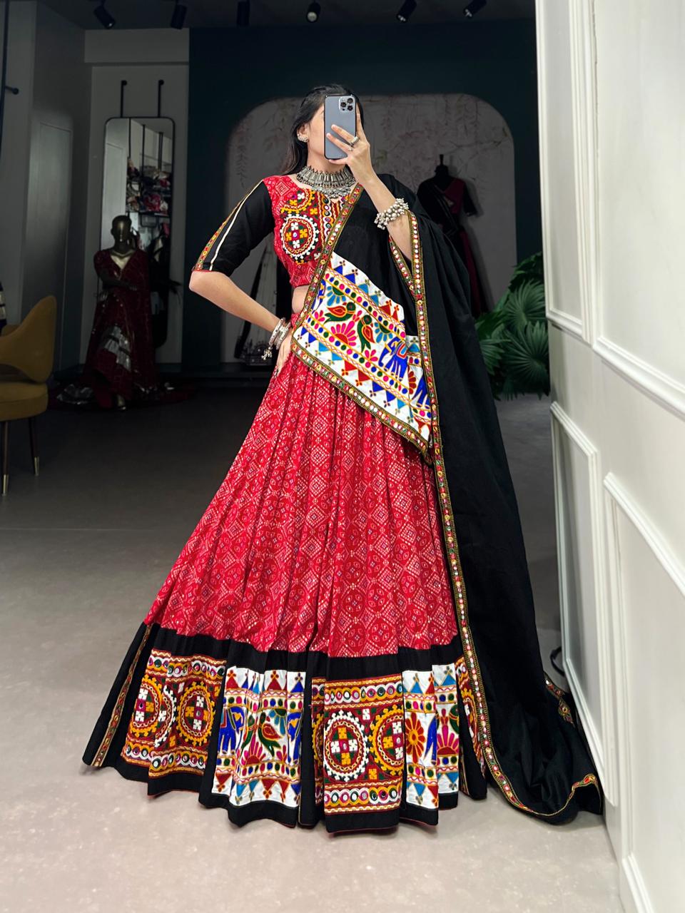 Person wearing a traditional red and black embroidered outfit in a room.