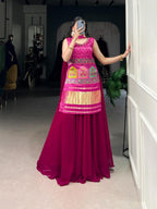 Model showcasing a premium pink Bandhani print sleeveless tunic kurti with multi-color traditional arch patchwork embroidery, heavy gold fringe hem, and solid flared pink georgette sharara pants inside a boutique.