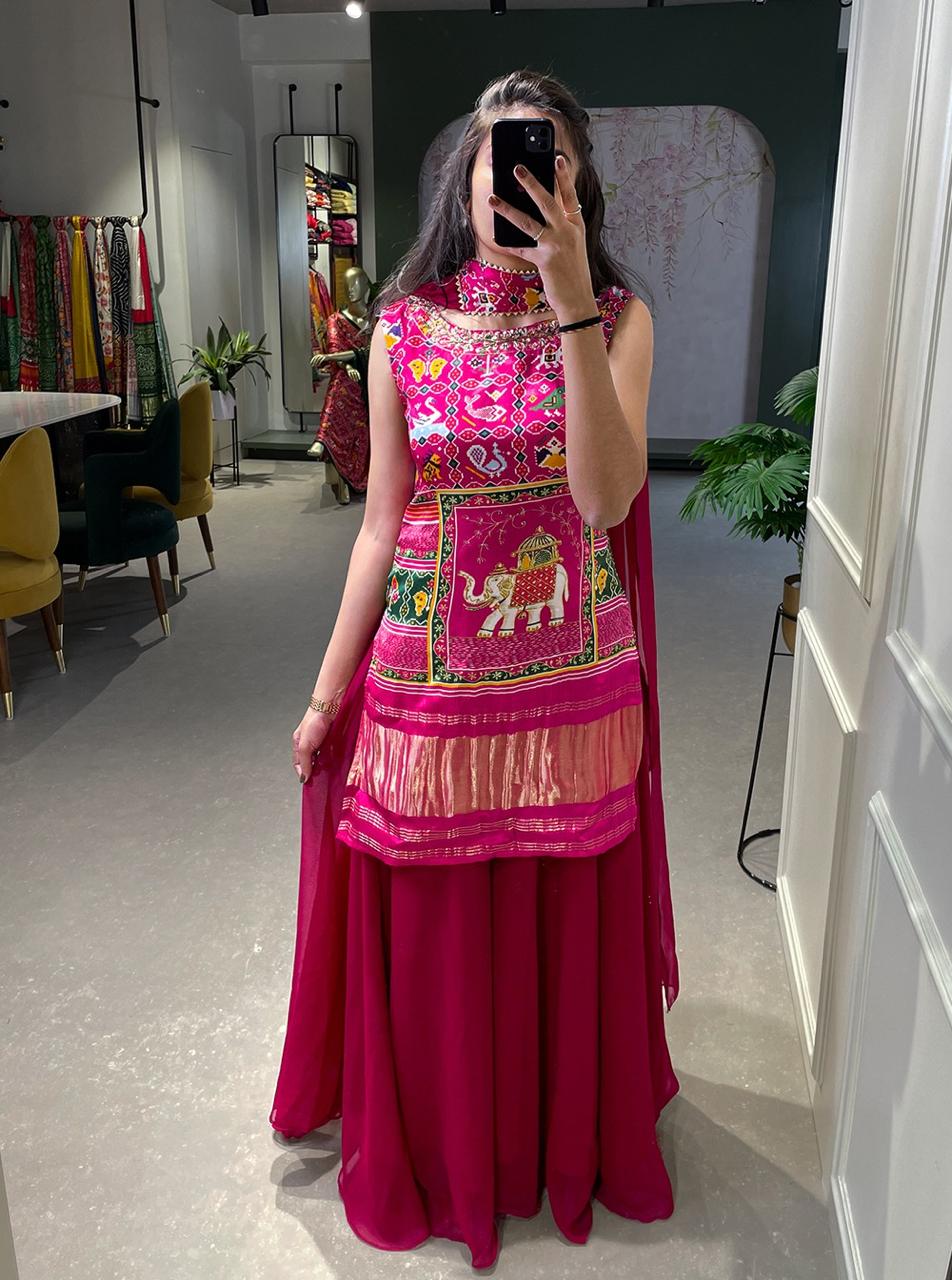 Model showcasing a premium pink Patola print long sleeveless tunic kurti with a heavy hand-embroidered royal elephant motif panel and a matching flared solid pink sharara pant inside a boutique. Main image